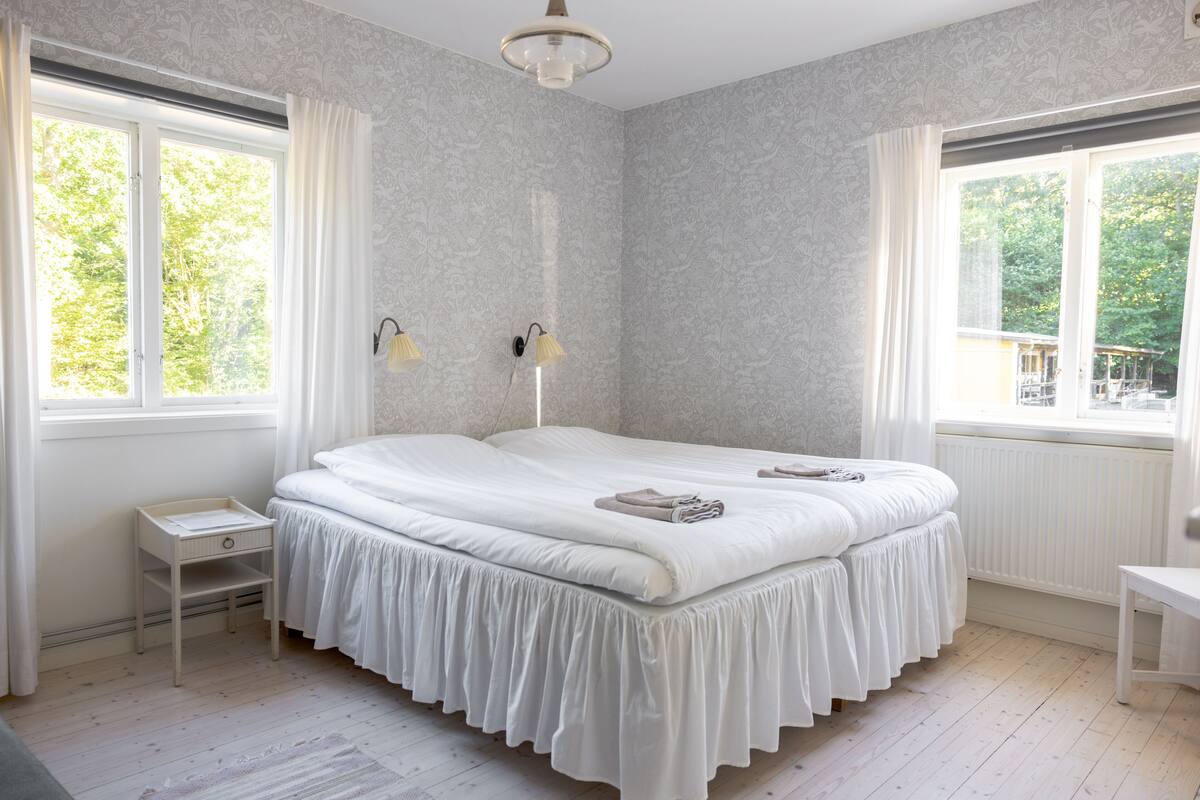Een slaapkamer met een groot bed, twee nachtkastjes, een raam met gordijnen en een radiator.