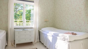 A bedroom with a single bed, a nightstand, a dresser, and a window with a view of trees.