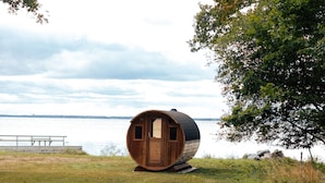 A cylindrical wooden structure with a door and windows, situated on a grassy area near a body of water. - Pensionat Strandhagen (Farjestaden)