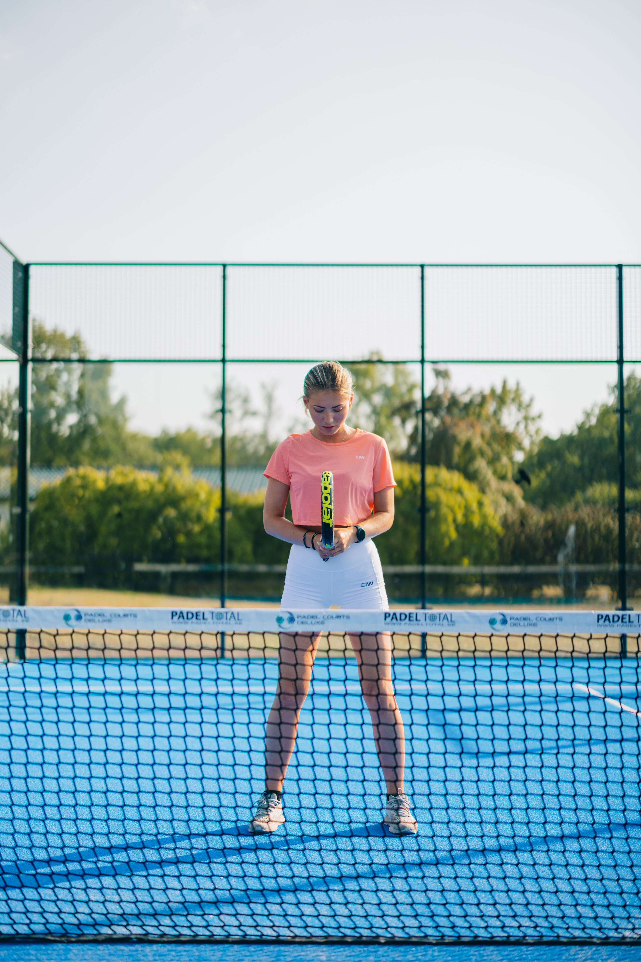A tennis court with a net, surrounded by a green fence.