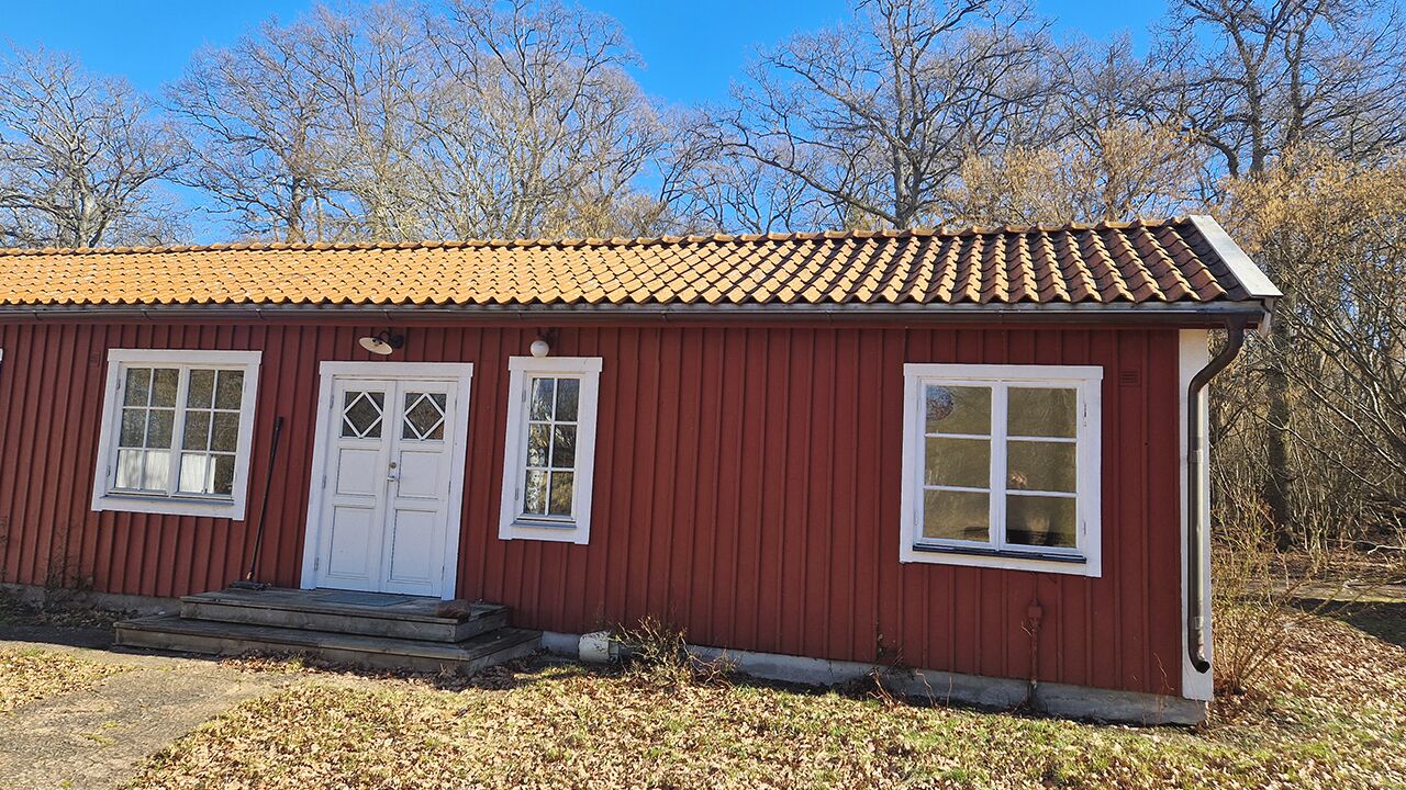 Un edificio di legno rosso con tetto in tegole, due finestre con cornice bianca e una porta bianca.