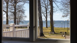 A window view of a park with a white fence, trees, and a body of water. - Pensionat Strandhagen (Farjestaden)
