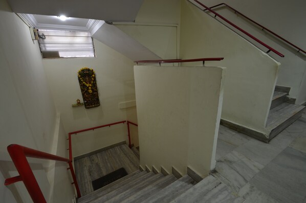 A staircase with red handrails, a small window with blinds, and a decorative floral arrangement on the wall.