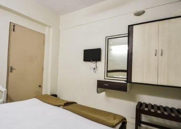 A hotel room with a bed, a small desk, a chair, a wardrobe, and a television.