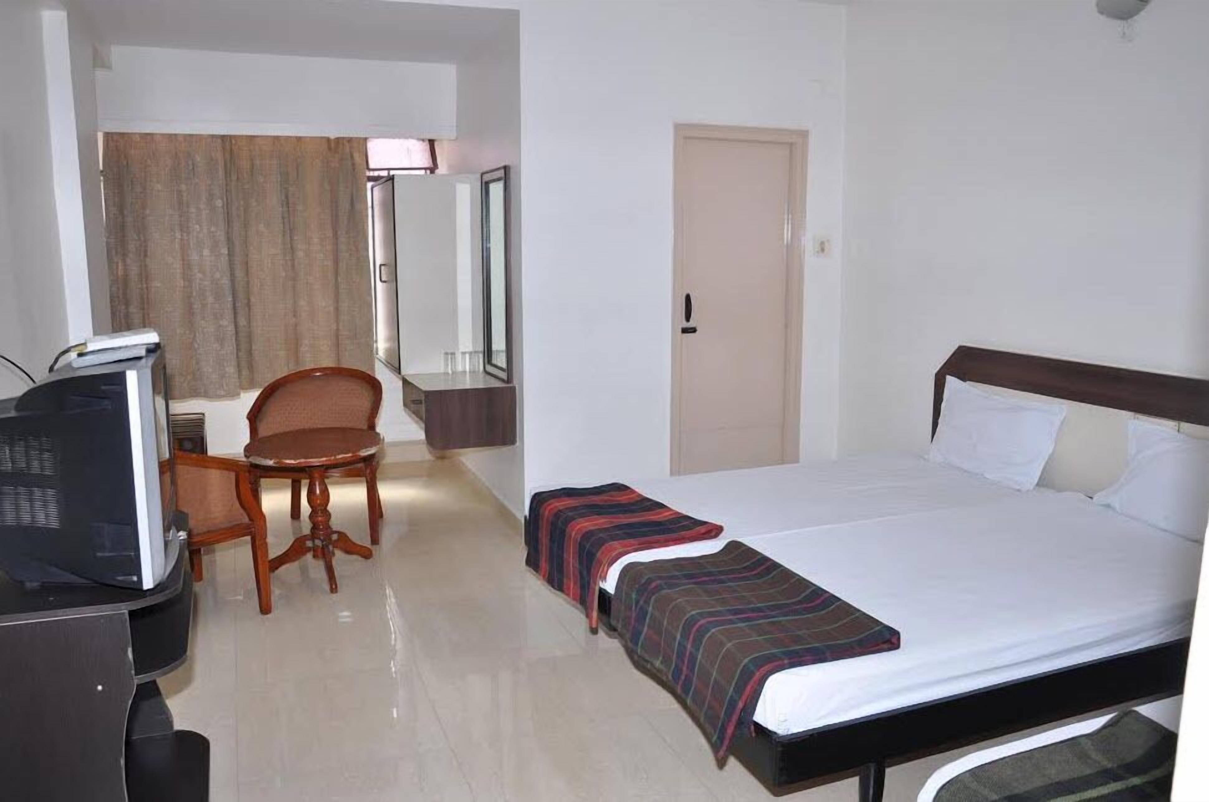 Habitación de hotel con una cama, un escritorio con computadora, una silla y una puerta.
