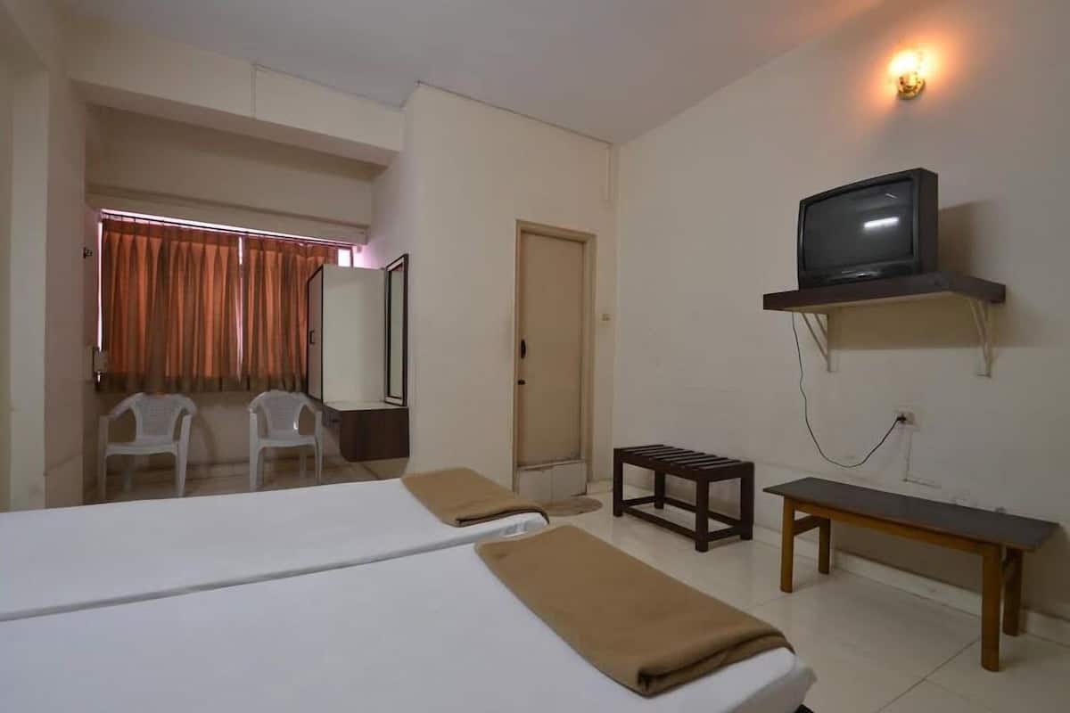 Habitación de hotel con cama, televisor montado en la pared, una mesita pequeña y dos sillas.
