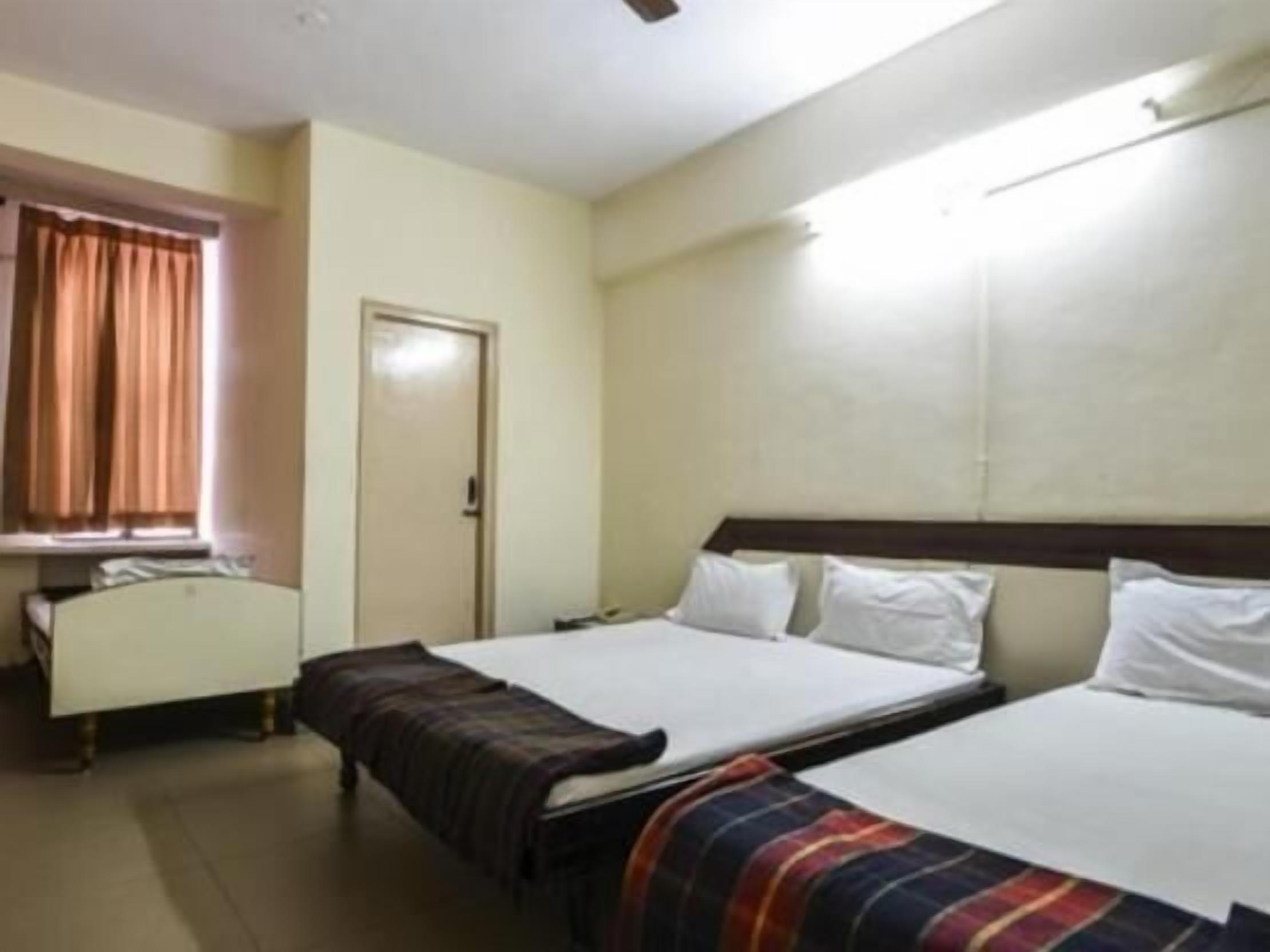 A hotel room with two beds, a window with curtains, a door, and a bedside table.