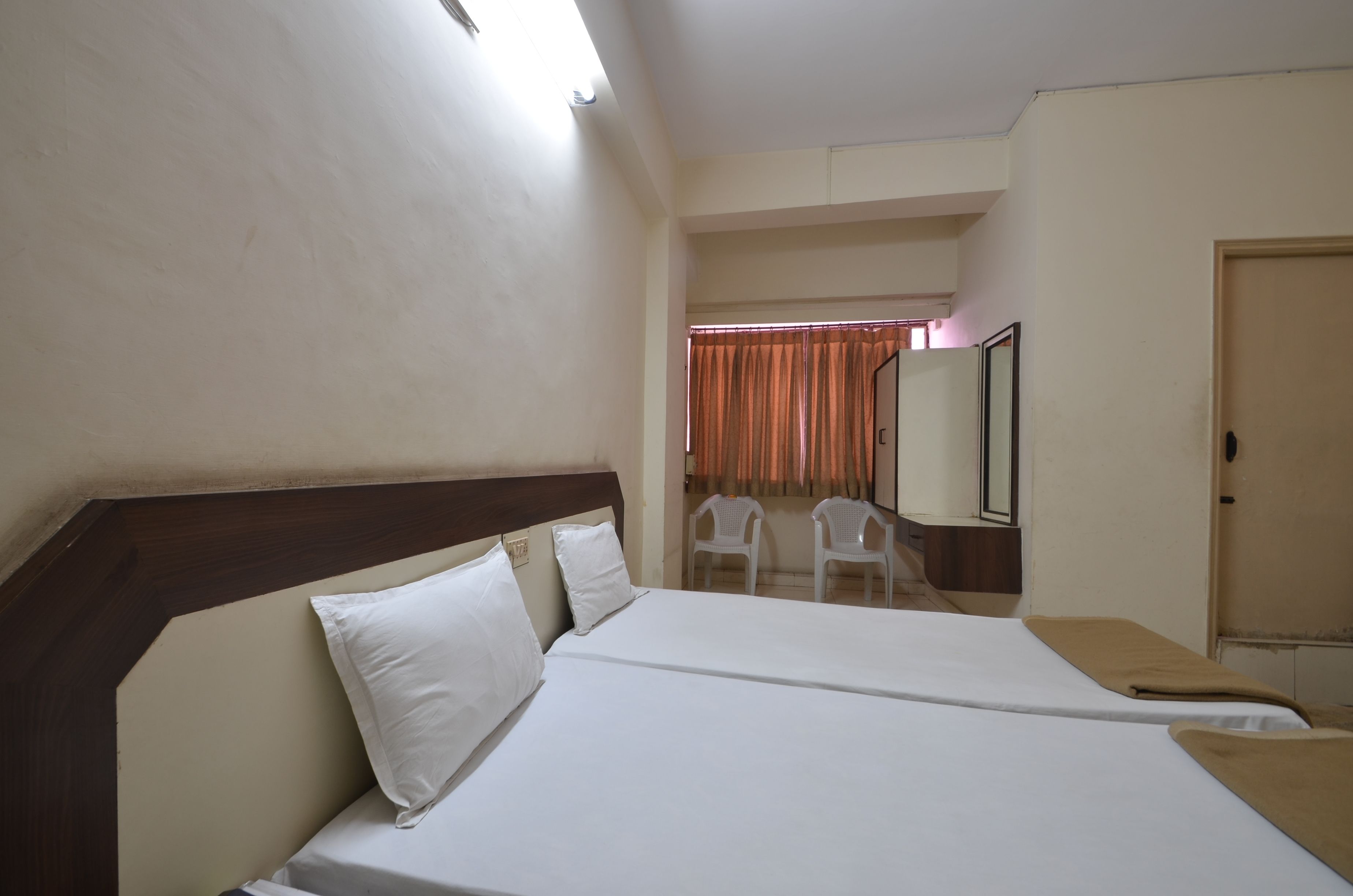 A hotel room with a bed, two white chairs, a mirror, and a door.