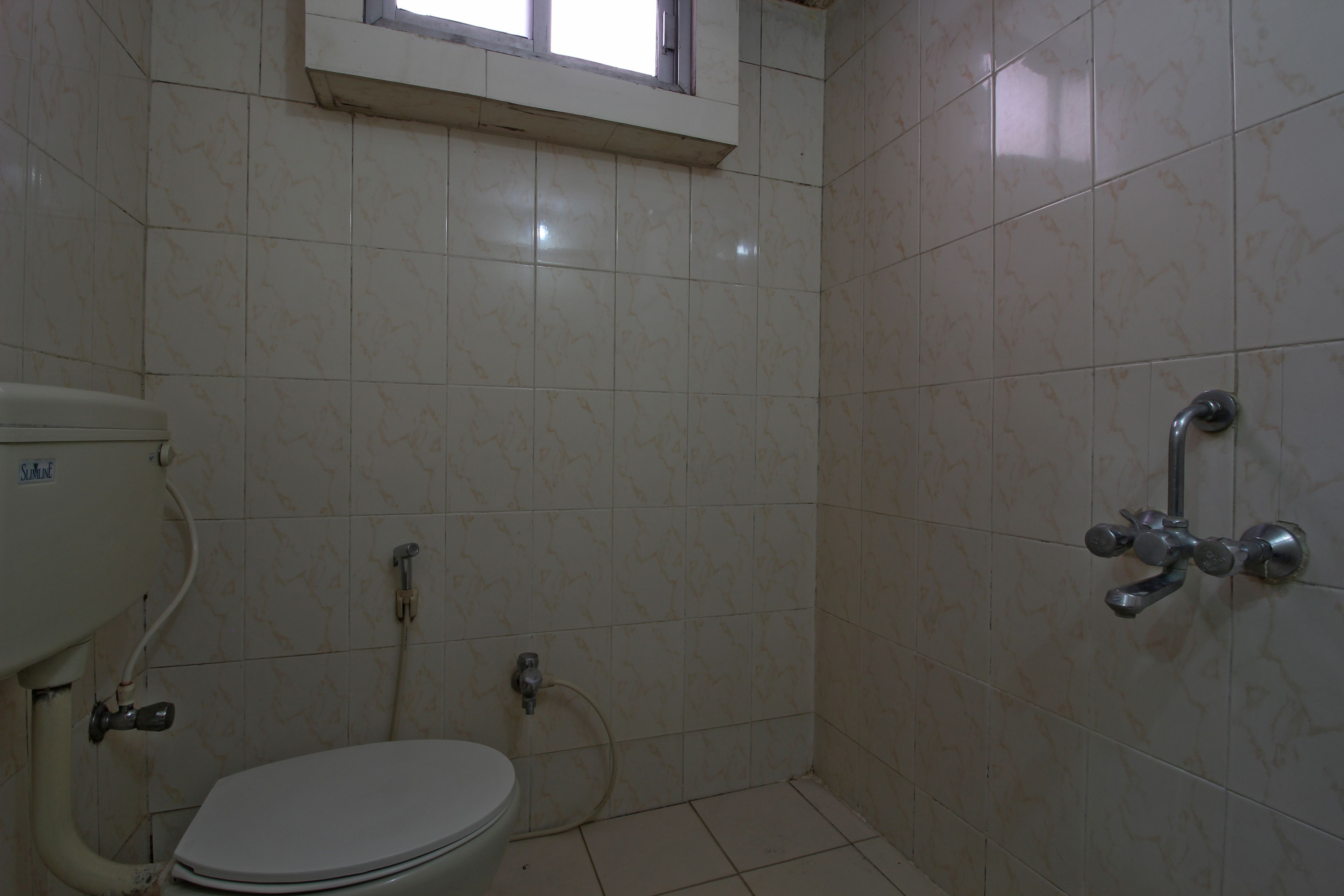 Um banheiro pequeno com azulejos, vaso sanitário, chuveiro e uma janela sobre o vaso.