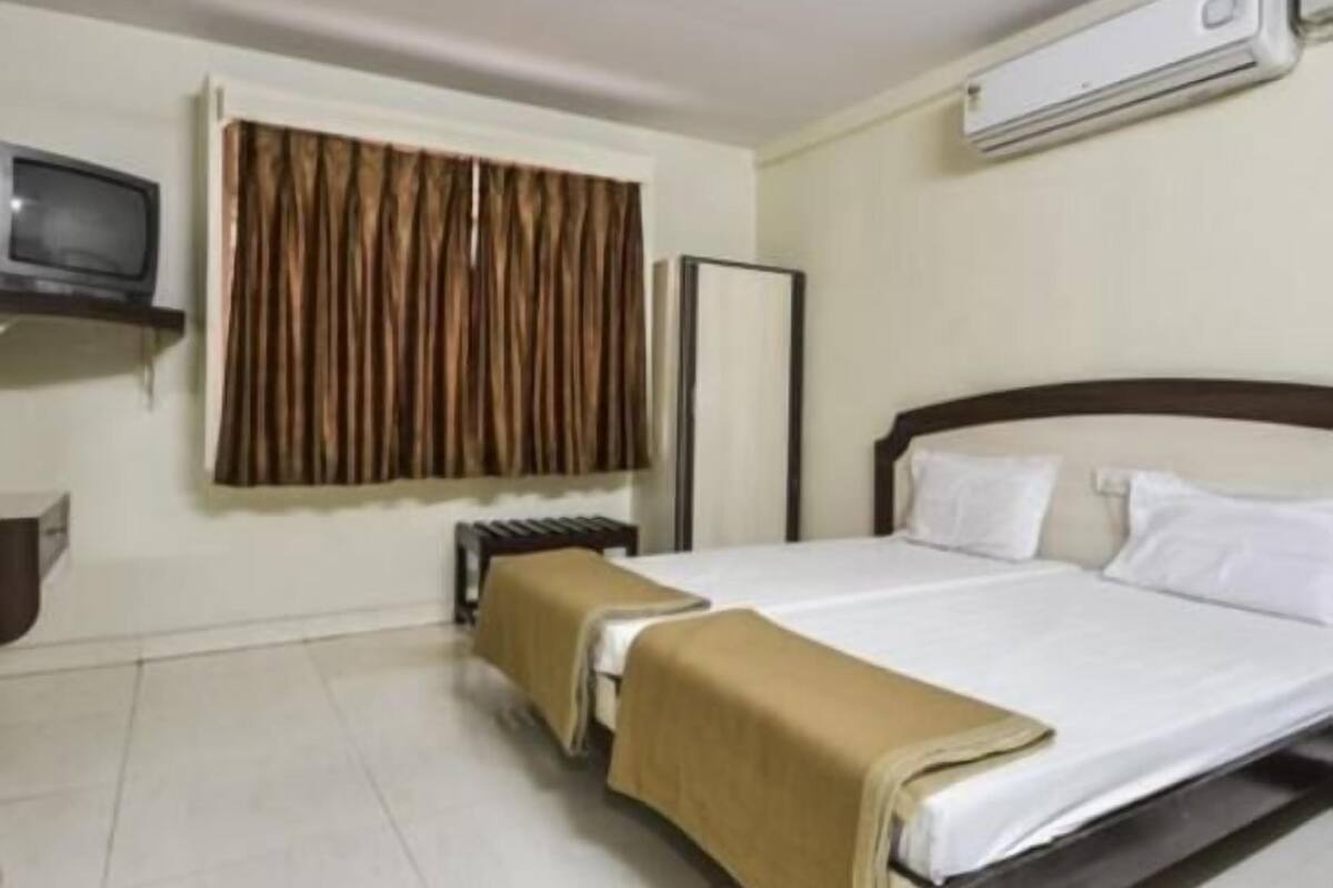 Una habitación de hotel con cama, televisión, aire acondicionado y ventana con cortinas.