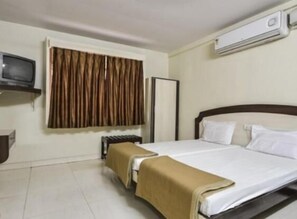 Una habitación de hotel con cama, televisión, aire acondicionado y ventana con cortinas.
