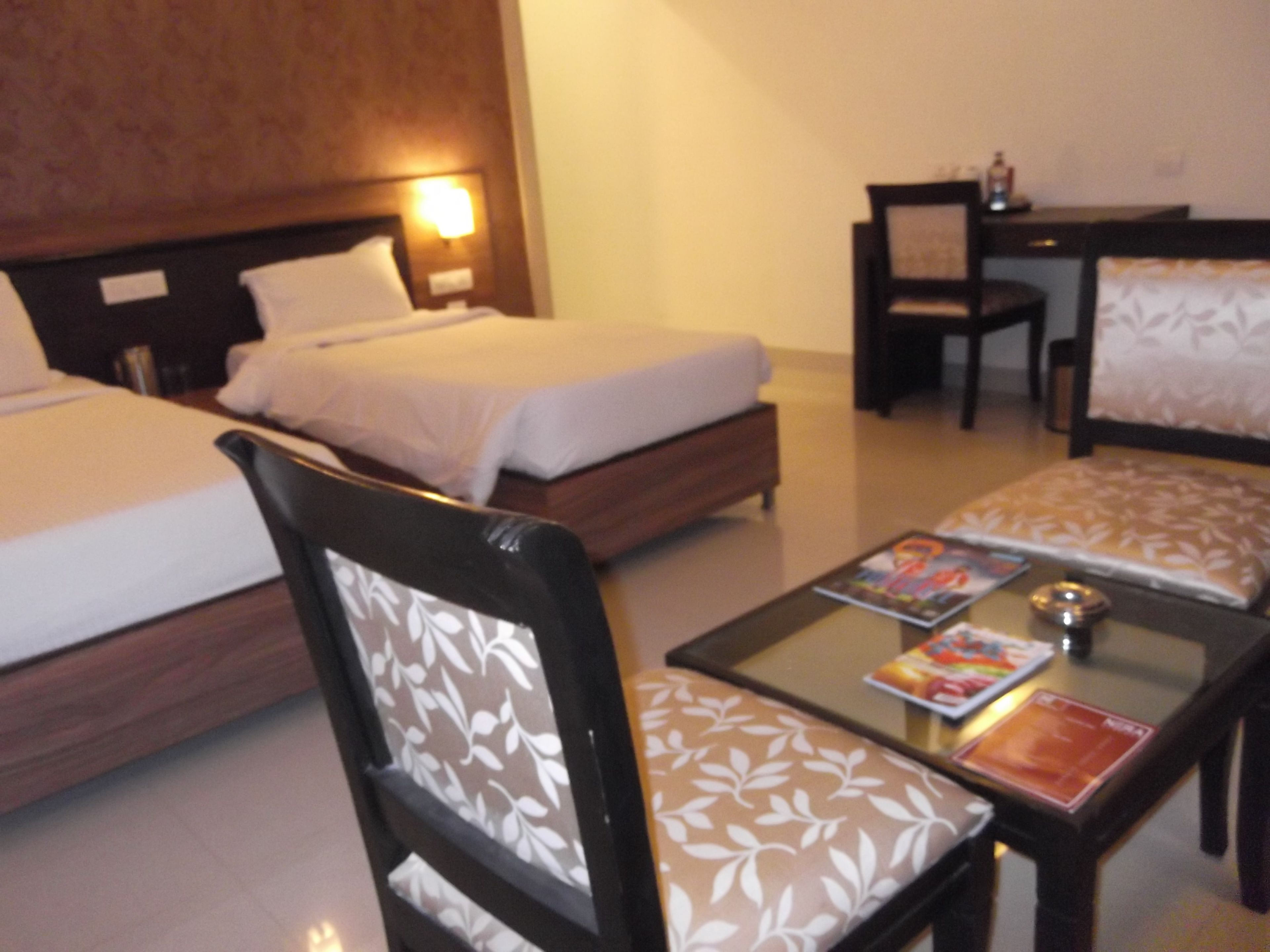 A hotel room with two beds, a desk, a chair, and a coffee table with magazines.