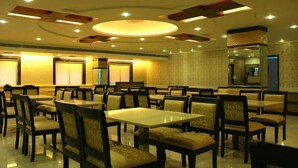 A spacious dining area with multiple tables and chairs, featuring a modern ceiling design with recessed lighting and a central circular light fixture. - Hotel Nera Regency (Hyderabad)