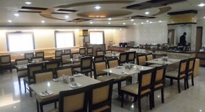 A spacious dining area with multiple tables and chairs, arranged in a linear fashion. - Hotel Nera Regency (Hyderabad)