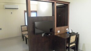 A compact room with a dark wooden desk, a flat-screen TV, a chair, and a small table with a kettle and water bottle. - Hotel Nera Regency (Hyderabad)