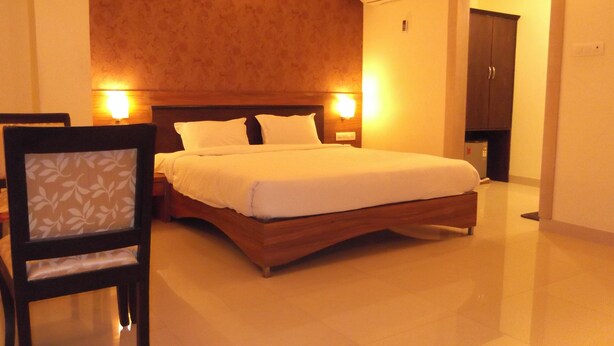 A neatly made bed with a wooden headboard, two bedside lamps, and an air conditioning unit on the wall. - Hotel Nera Regency (Hyderabad)