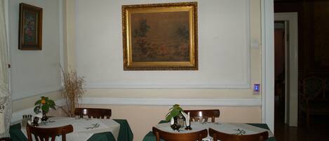 Une salle à manger avec une table dressée pour quatre personnes, un tableau encadré au mur et une porte donnant sur une autre pièce.