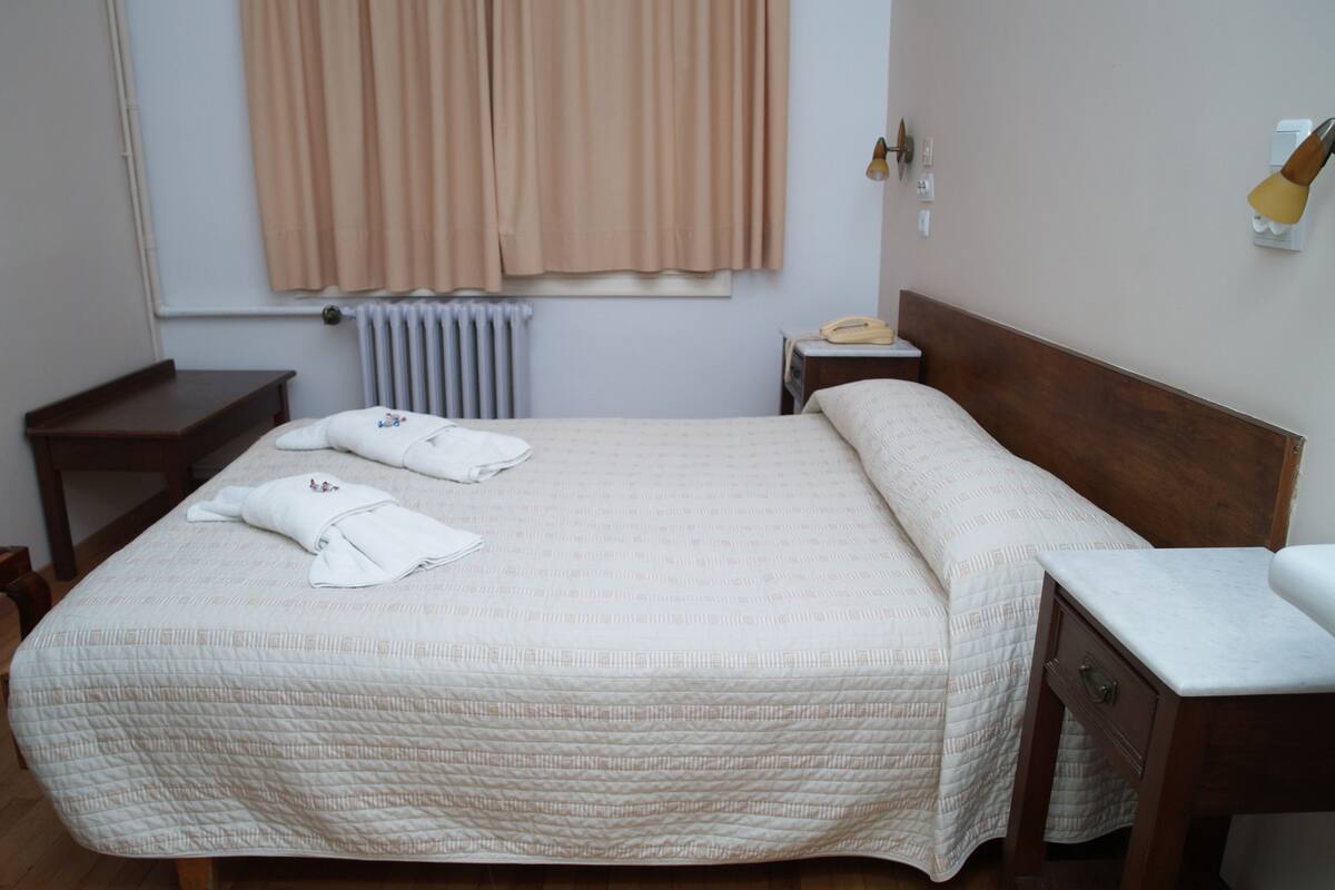 A neatly made bed with a quilted bedspread, a wooden nightstand with a lamp, and a wooden dresser with a mirror.