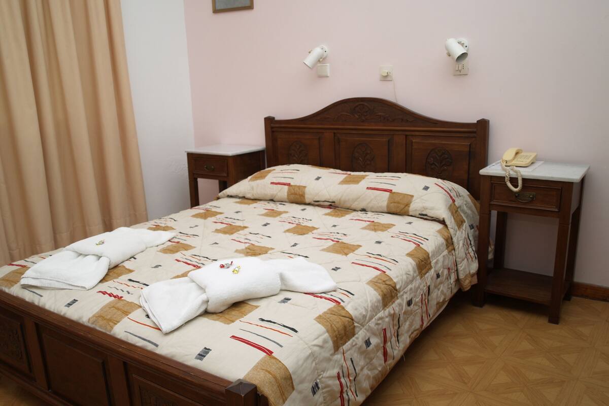 A neatly made bed with a patterned bedspread, two bedside tables with lamps, and a telephone on one of the tables.