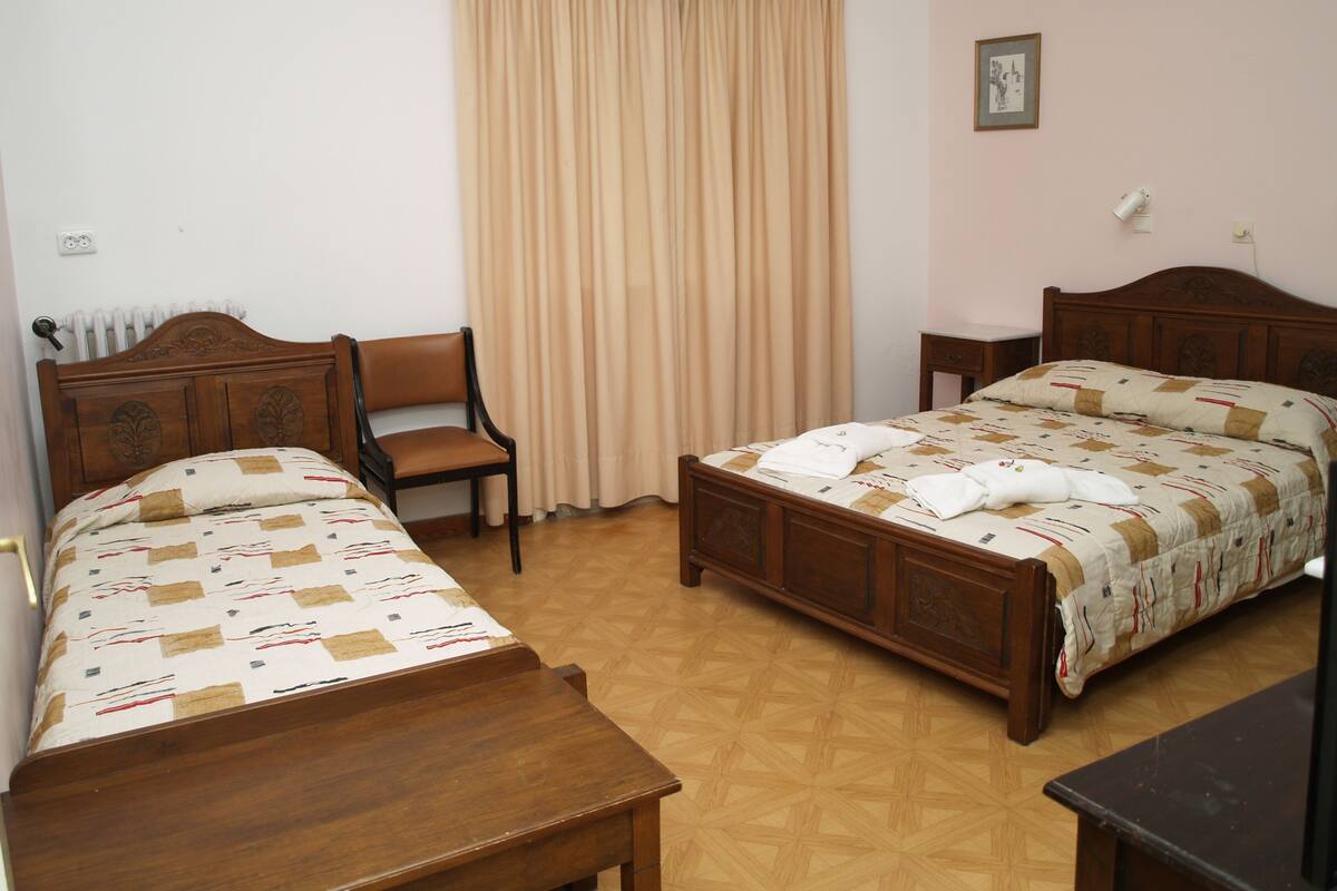 A bedroom with two wooden beds, a chair, a bedside table, and a window with curtains.