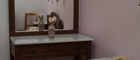 A wooden vanity with a mirror, two floral vases, a telephone, and a small stool.