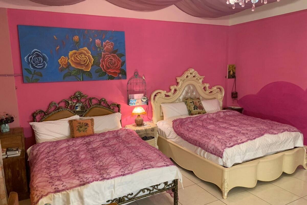 Una habitación con dos camas, paredes rosas y un cuadro de rosas.