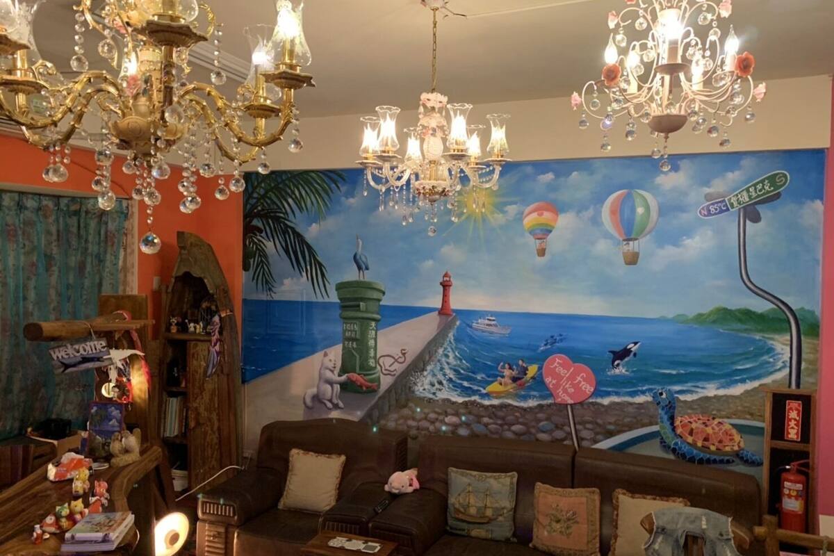 Un salón acogedor con un mural de una escena de playa, un sofá marrón, una mesita de madera y una araña.
