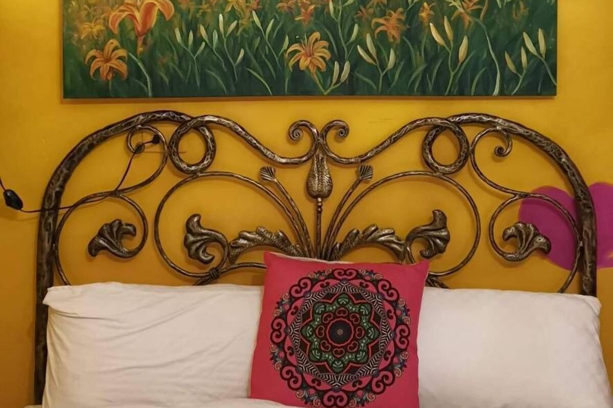 Una cama con cabecera metálica, ropa de cama blanca y una almohada con estampado rojo.