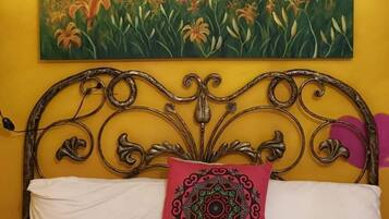 A bed with a metal headboard, white bedding, and a red patterned pillow.