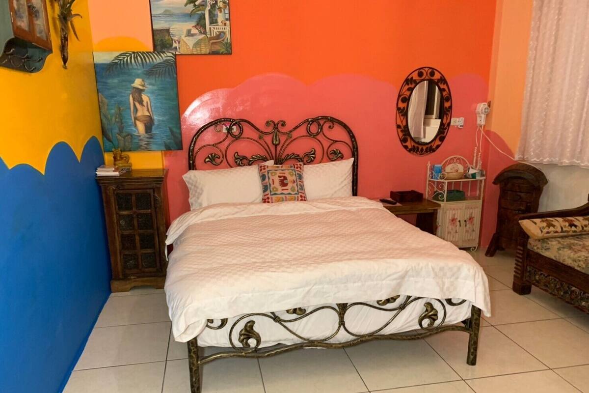 Una cama con estructura metálica y ropa de cama blanca en una habitación con pared rosa y una pared de acento azul.