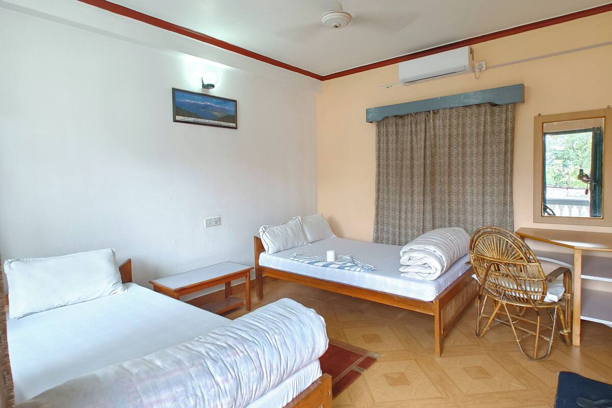 Une chambre d’hôtel avec deux lits simples, un bureau en bois, une chaise en osier et une fenêtre avec des rideaux.