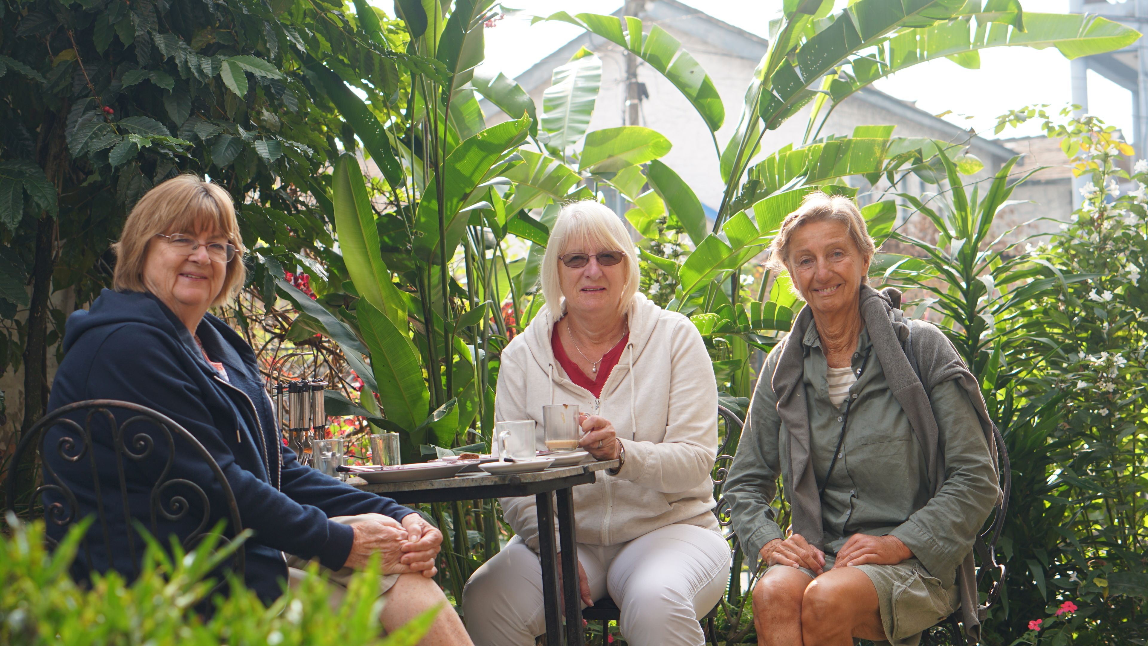 Tres personas sentadas en una mesa al aire libre, rodeadas de abundante vegetación.