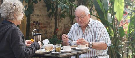 Two people dining at an outdoor table with a rustic brick wall and greenery in the background.