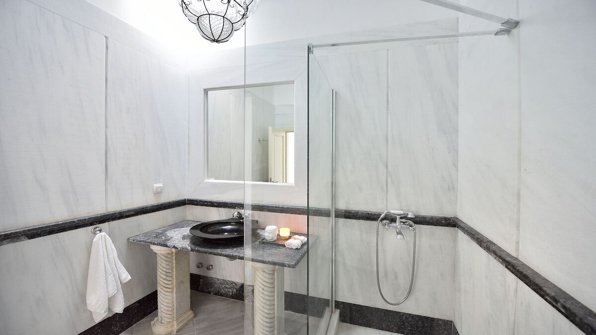 A modern bathroom with a marble vanity, a glass shower enclosure, and a large mirror.