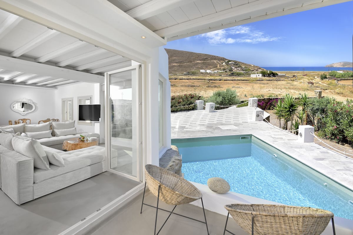 Un salon moderne avec un canapé blanc, un téléviseur à écran plat et une vue sur une piscine et un paysage.