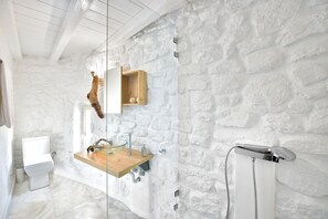 Un baño con pared de piedra, un estante de madera con espejo, inodoro y ducha.