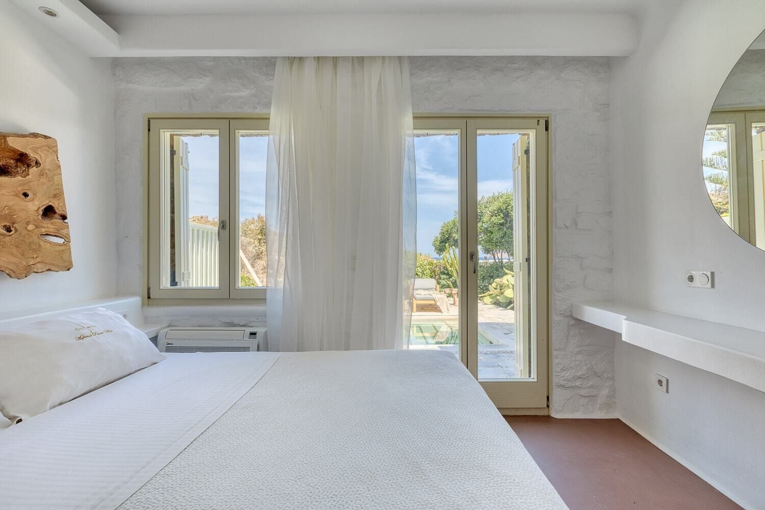 Un dormitorio con una cama grande, una puerta corrediza al balcón y vistas al verdor exterior.