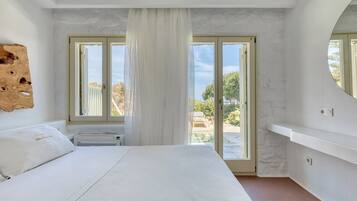 Un dormitorio con una cama grande, una puerta corrediza al balcón y vistas al verdor exterior.