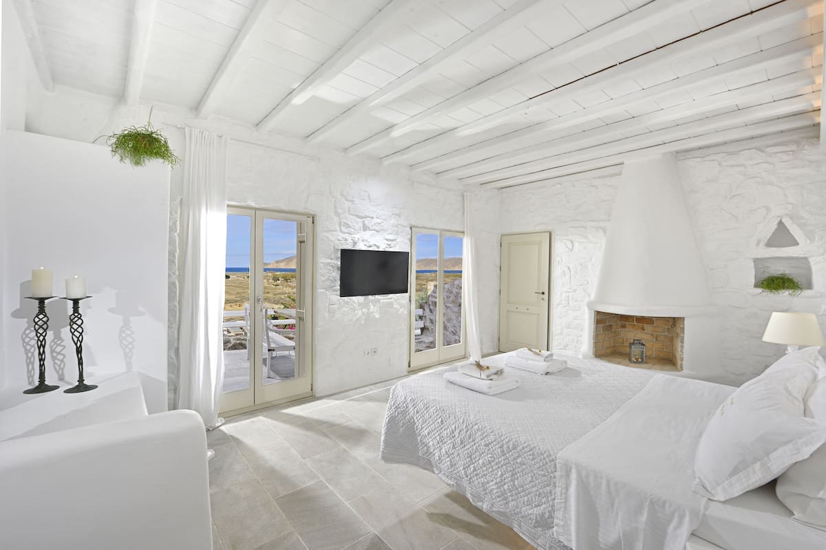 Une chambre à coucher décorée dans des tons de blanc, avec un lit, une cheminée et un téléviseur fixé au mur.