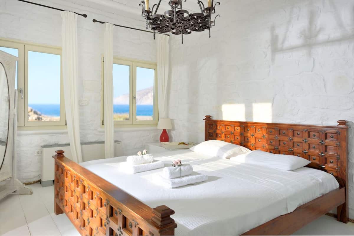 Une chambre avec un lit en bois, du linge de lit blanc, une vue sur la mer et un lustre.
