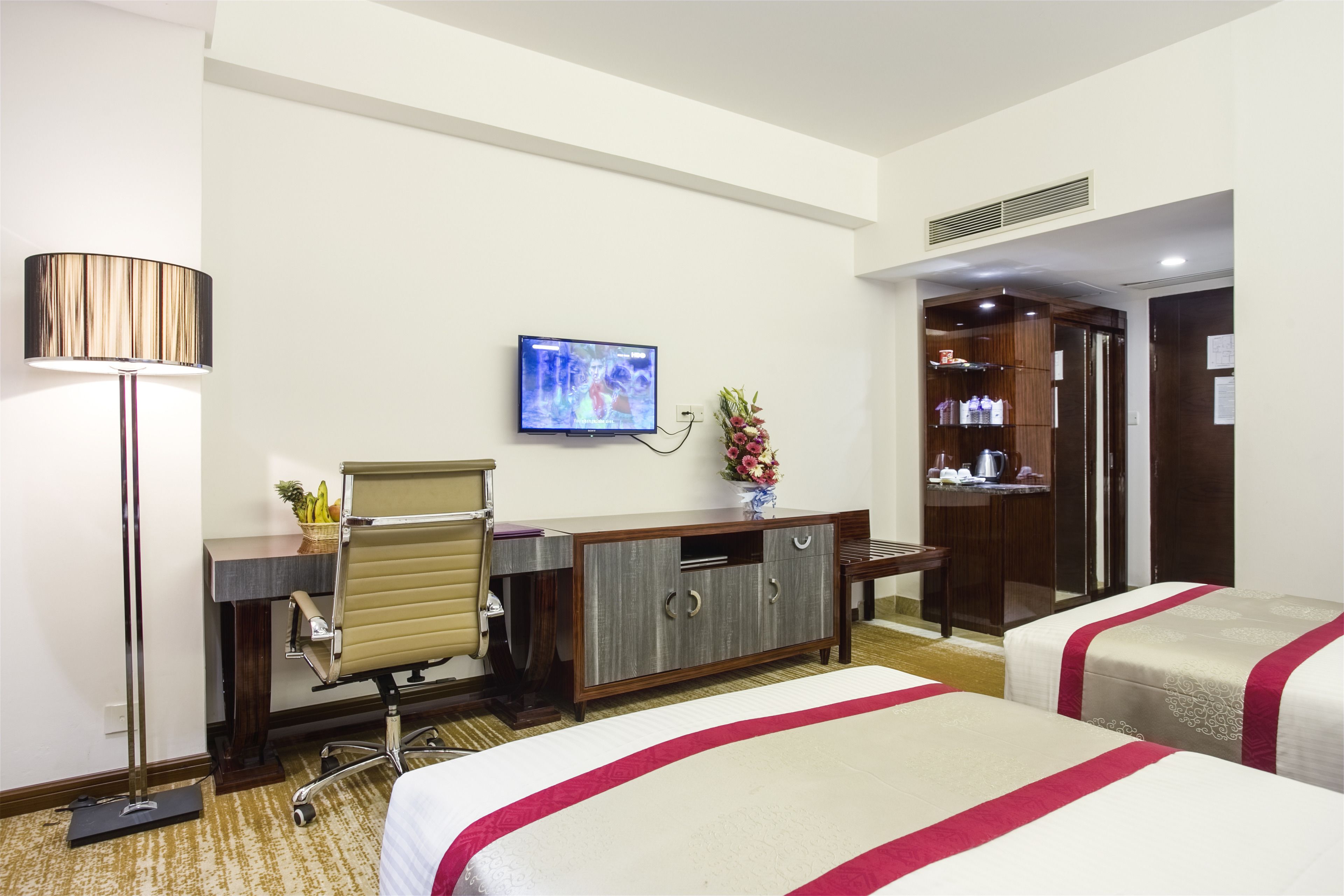A hotel room with a desk, two beds, a TV, a lamp, and a wardrobe.