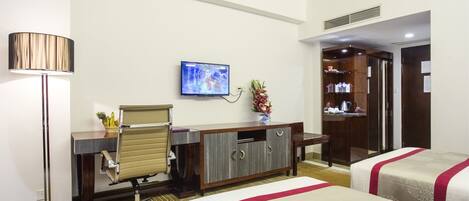 A hotel room with a desk, two beds, a TV, a lamp, and a wardrobe.