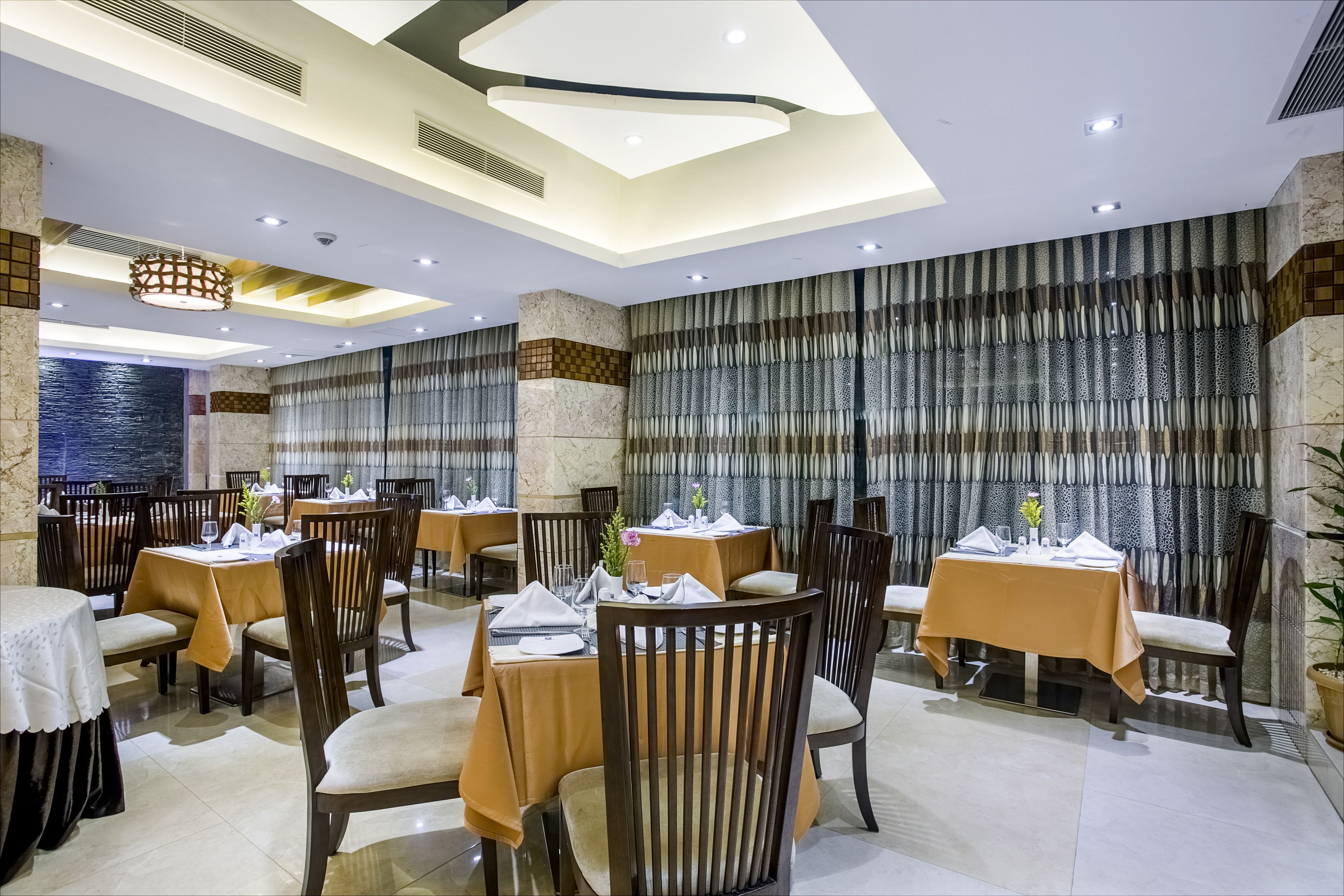 A restaurant with round tables, dark wooden chairs, and a modern ceiling design.