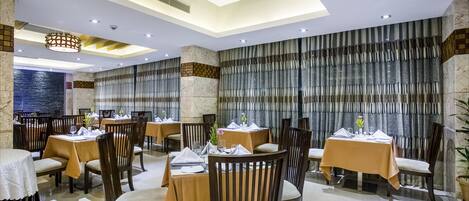 A restaurant with round tables, dark wooden chairs, and a modern ceiling design.