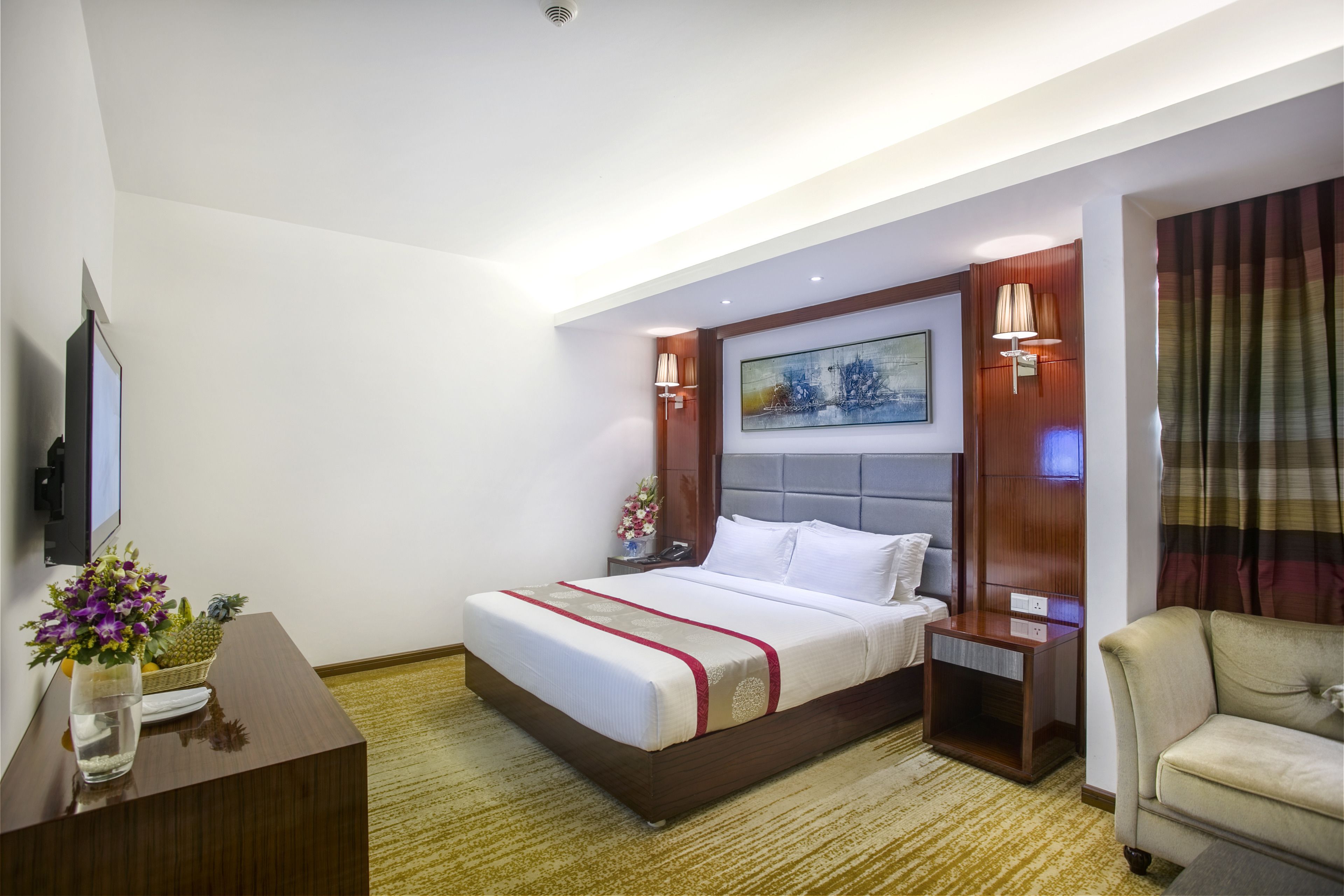 A hotel room with a large bed, a desk with a vase of flowers, a television, and a couch.