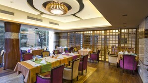 A dining area with multiple tables and chairs, a large decorative light fixture, and a view through a glass partition. - Hotel Bengal Blueberry (Dhaka)