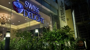 The exterior of the Swiss Delight hotel with a prominent sign, glass facade, and surrounding greenery. - Hotel Bengal Blueberry (Dhaka)