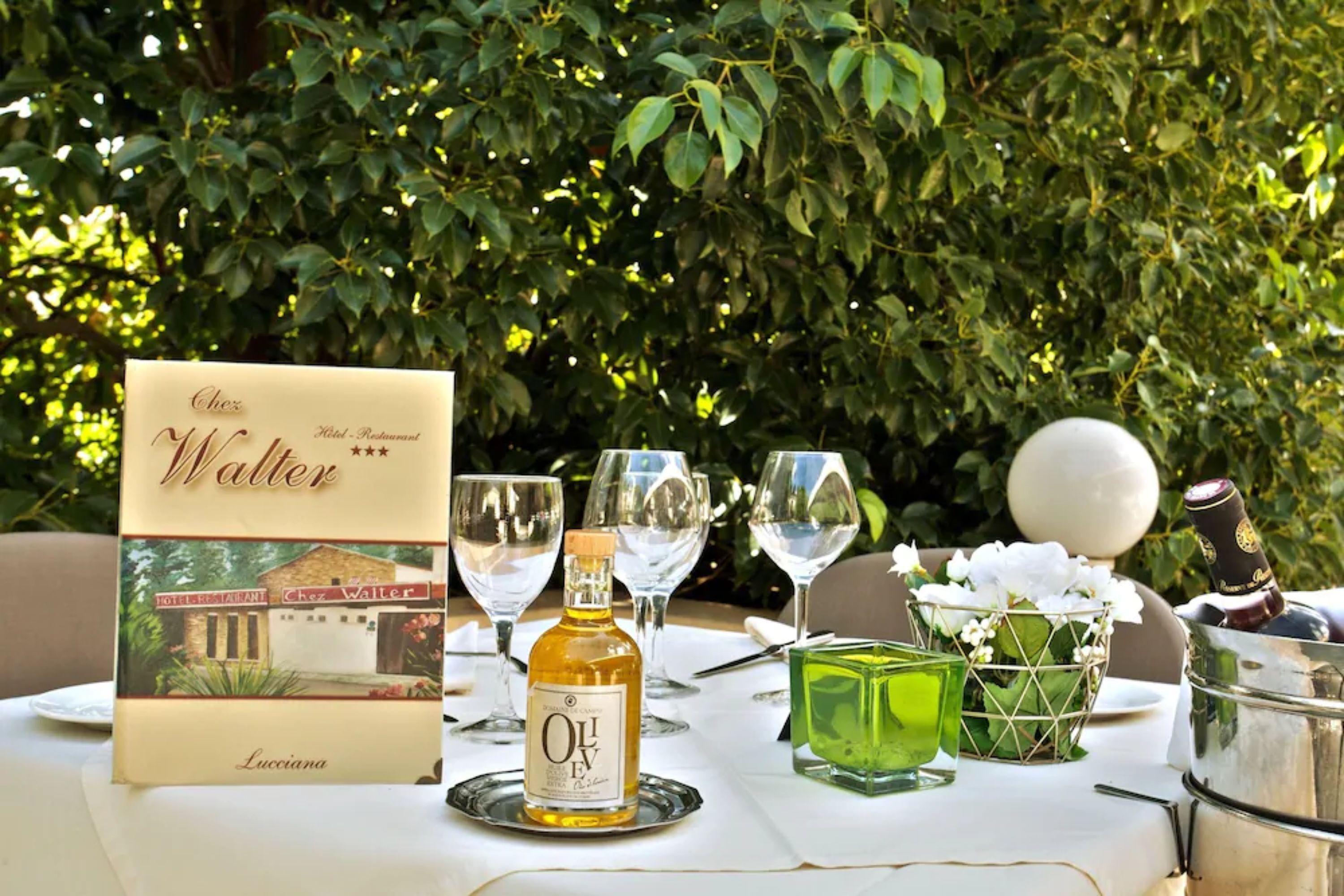 A table set outdoors with a bottle of olive oil, a menu, and glasses.