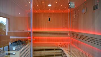 Uma sauna com divisória de vidro, ripas de madeira e luz vermelha.