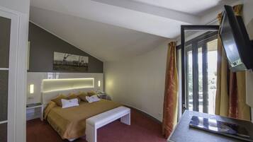 Una habitación de hotel moderna con una cama grande, un banco, un escritorio con televisor de pantalla plana y una ventana con cortinas.